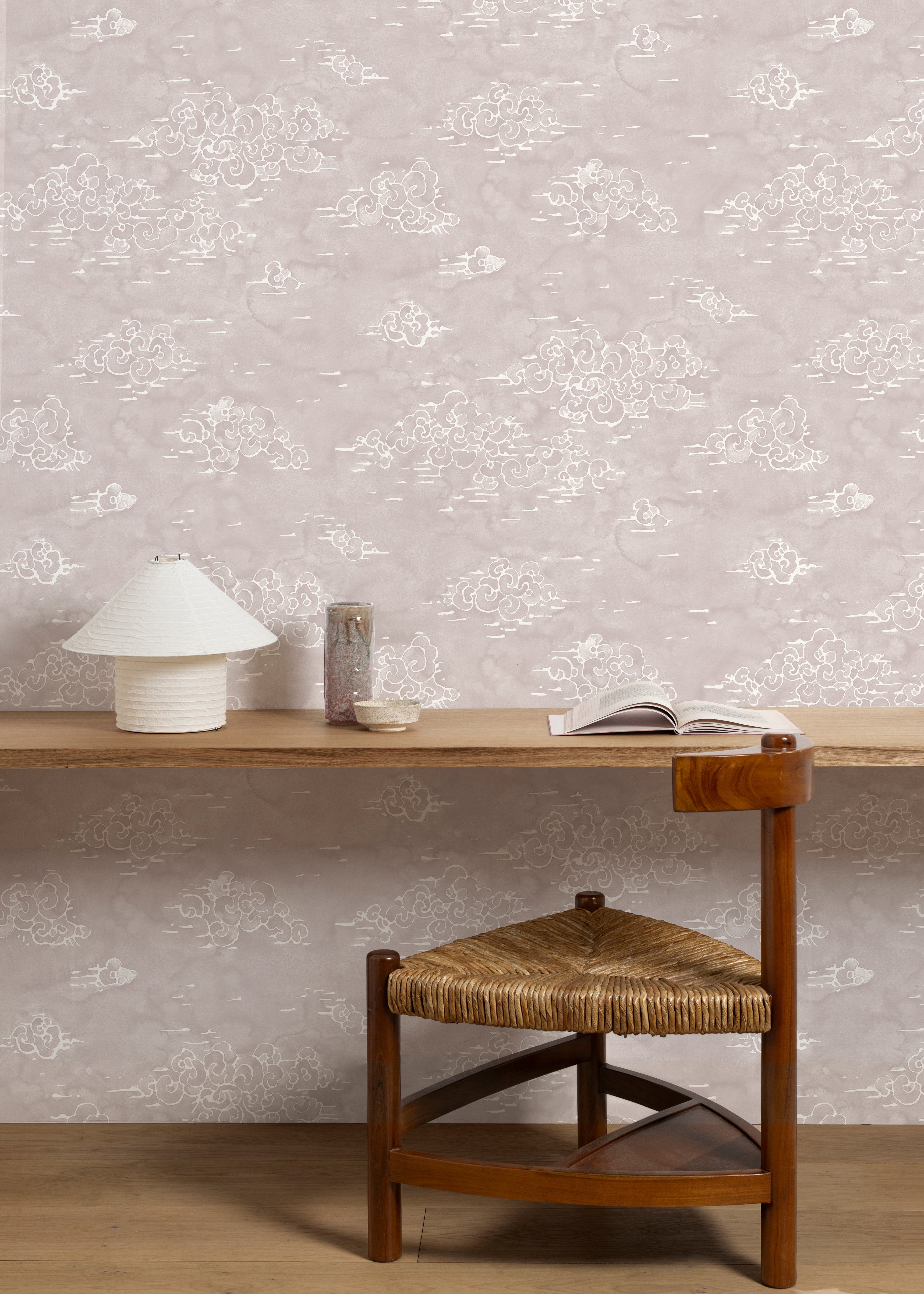 A wooden chair stands in wooden desk front of a wall papered in a painterly cloud pattern in white on a pastel purple field.