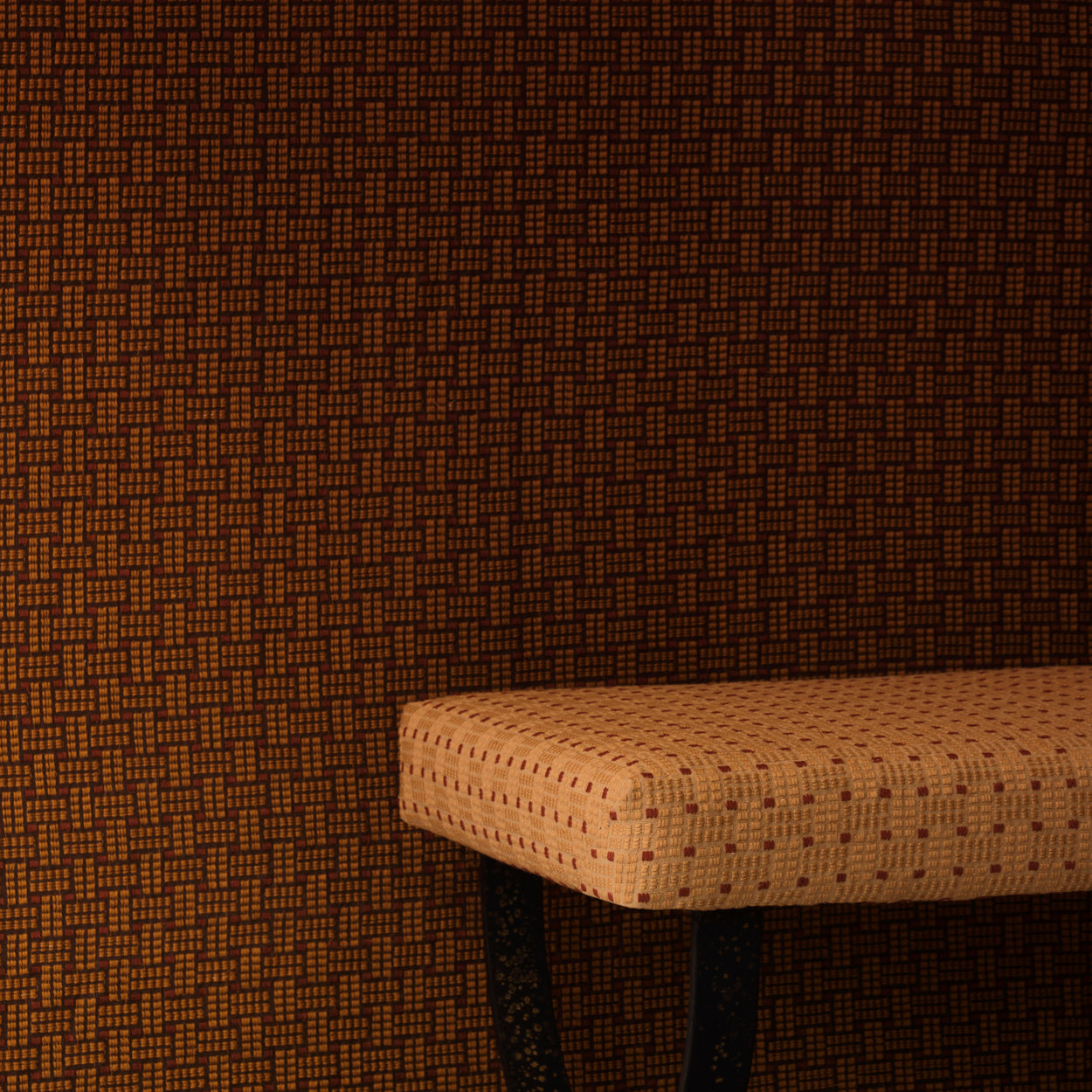 Settee bench with a warm beige embroidered upholstery in tan against a wall in the same design in a darker shade of brown. 