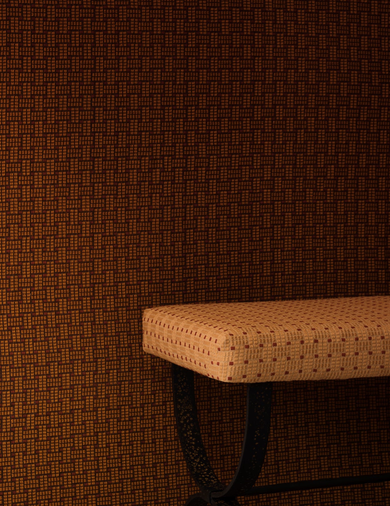 Settee bench with a warm beige embroidered upholstery in tan against a wall in the same design in a darker shade of brown. 