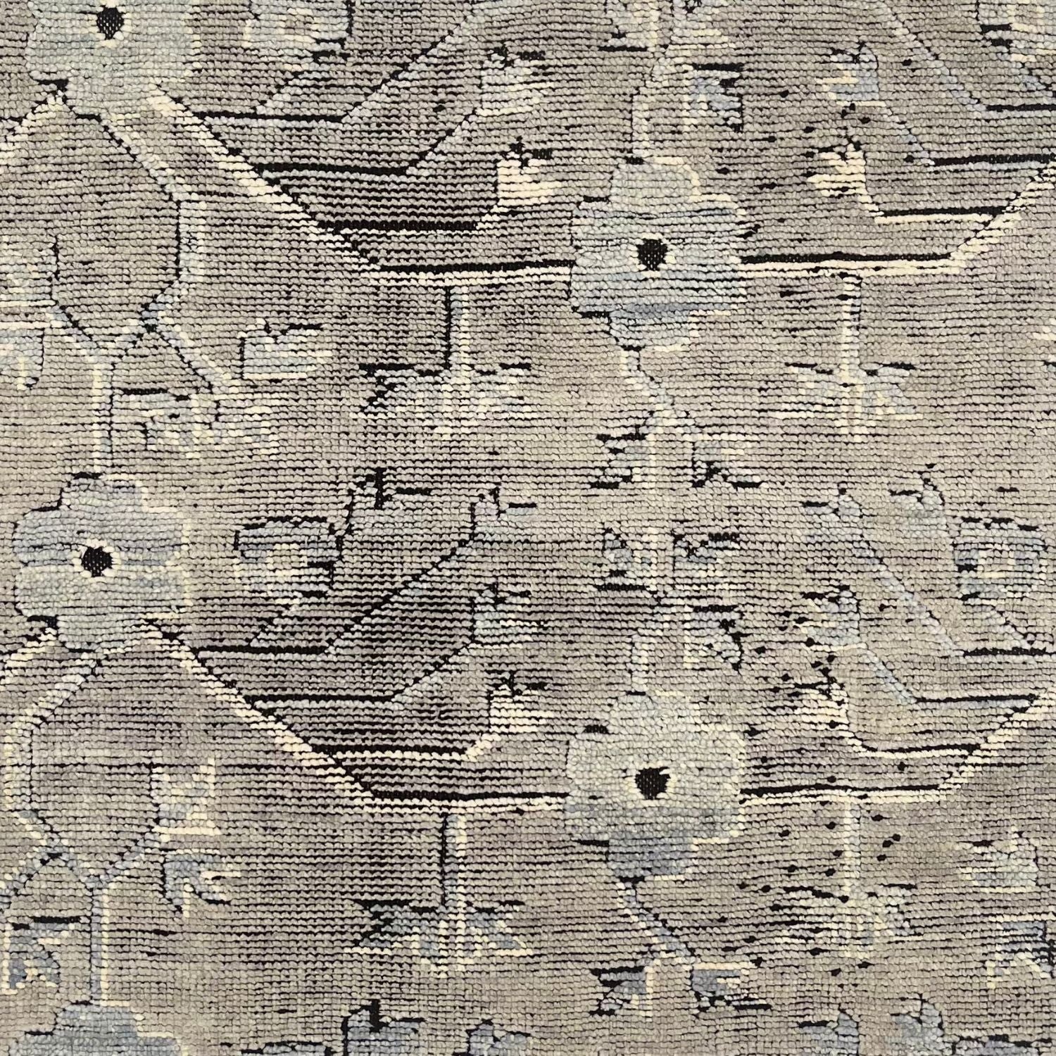 A rug with an overall flower and vine pattern in shades of pale grey, taupe, ivory, and black.
