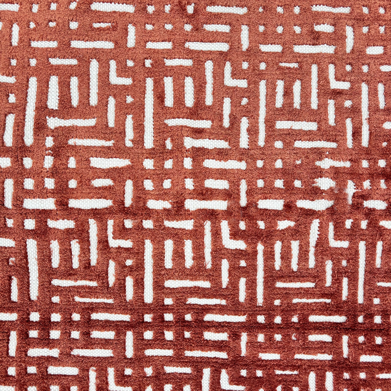 Handknotted rug sample with a geometric lattice pattern in rust red on a white field.