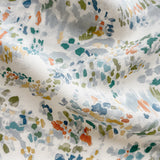 Draped fabric yardage in a painterly cloud print in shades of red, green, yellow and blue on a cream field.
