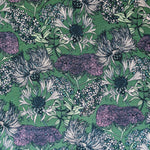 Detail of fabric in a dense floral print in shades of cream, purple and green on a green field.