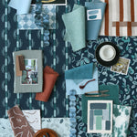 Collection of fabric swatches and samples arranged on a patterned surface in shades of teal, blue and rust. 