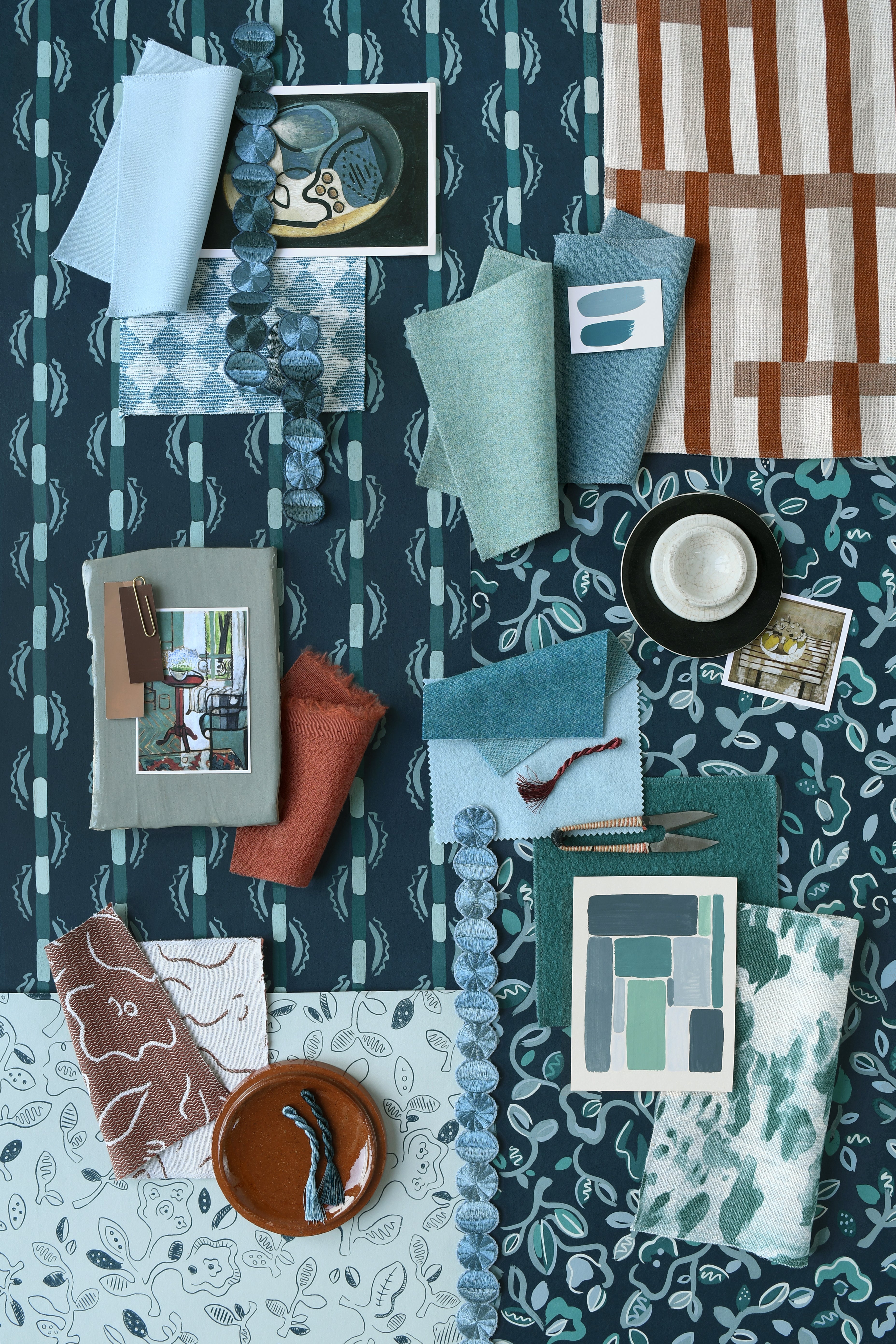 Collection of fabric swatches and samples arranged on a patterned surface in shades of teal, blue and rust. 