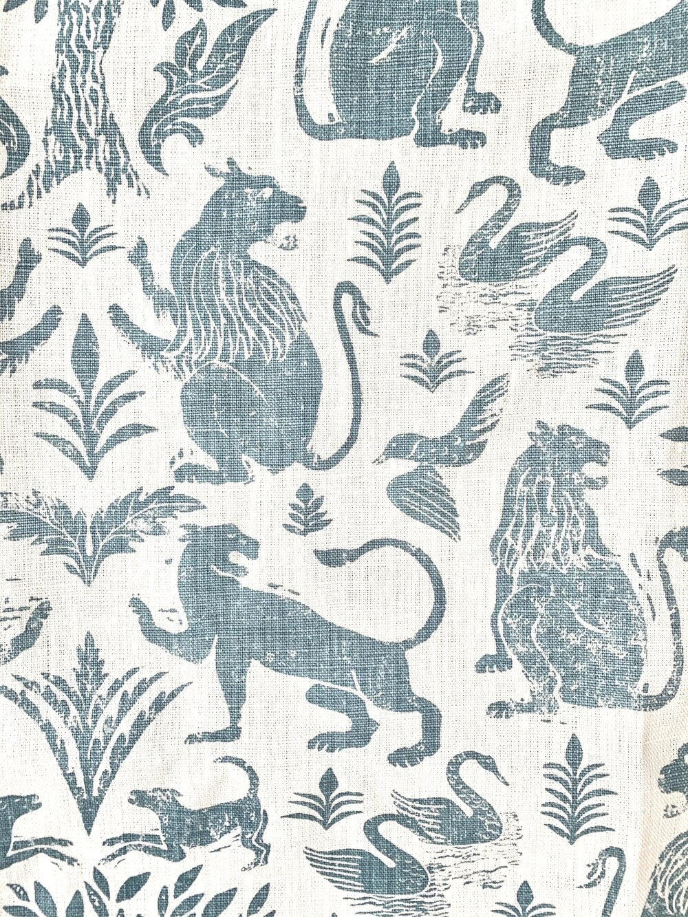 Close-up of fabric in a lion and plant print in blue-gray on a white field.