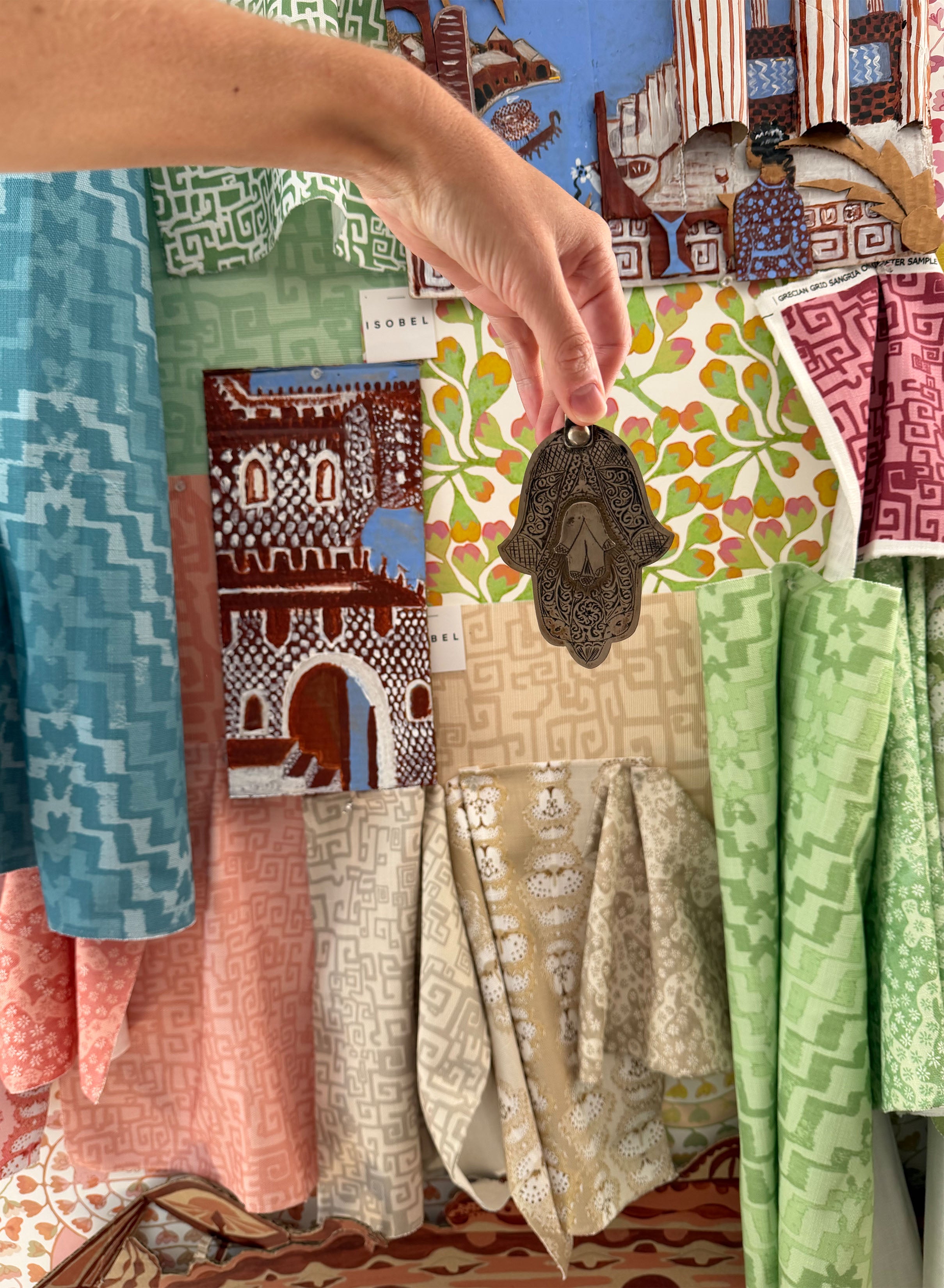 Moodboard with brightly colored fabric swatches and woman's arm holding an ornate metal charm. 
