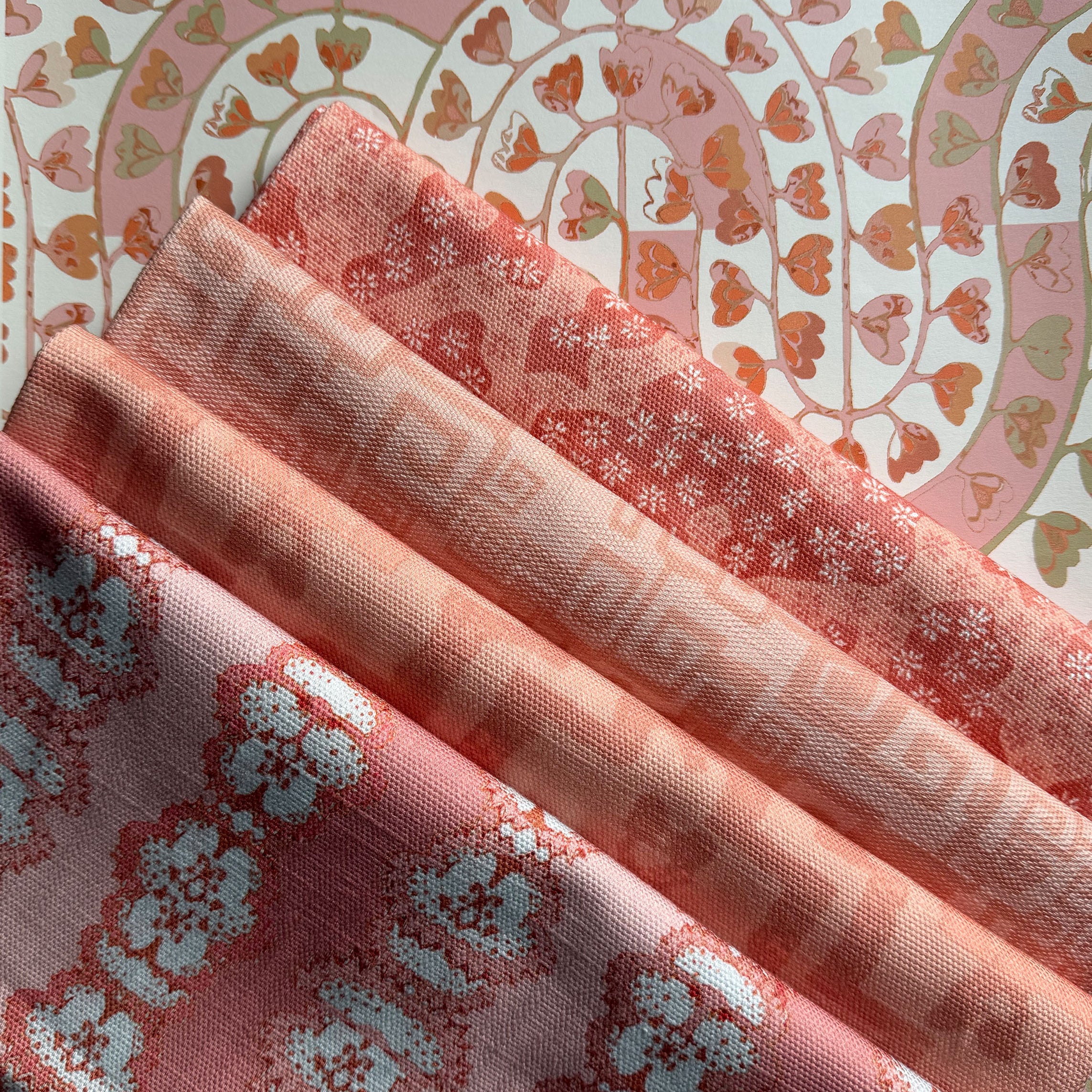 Stack of folded fabric swatches in various patterns in a soft pink palette. 