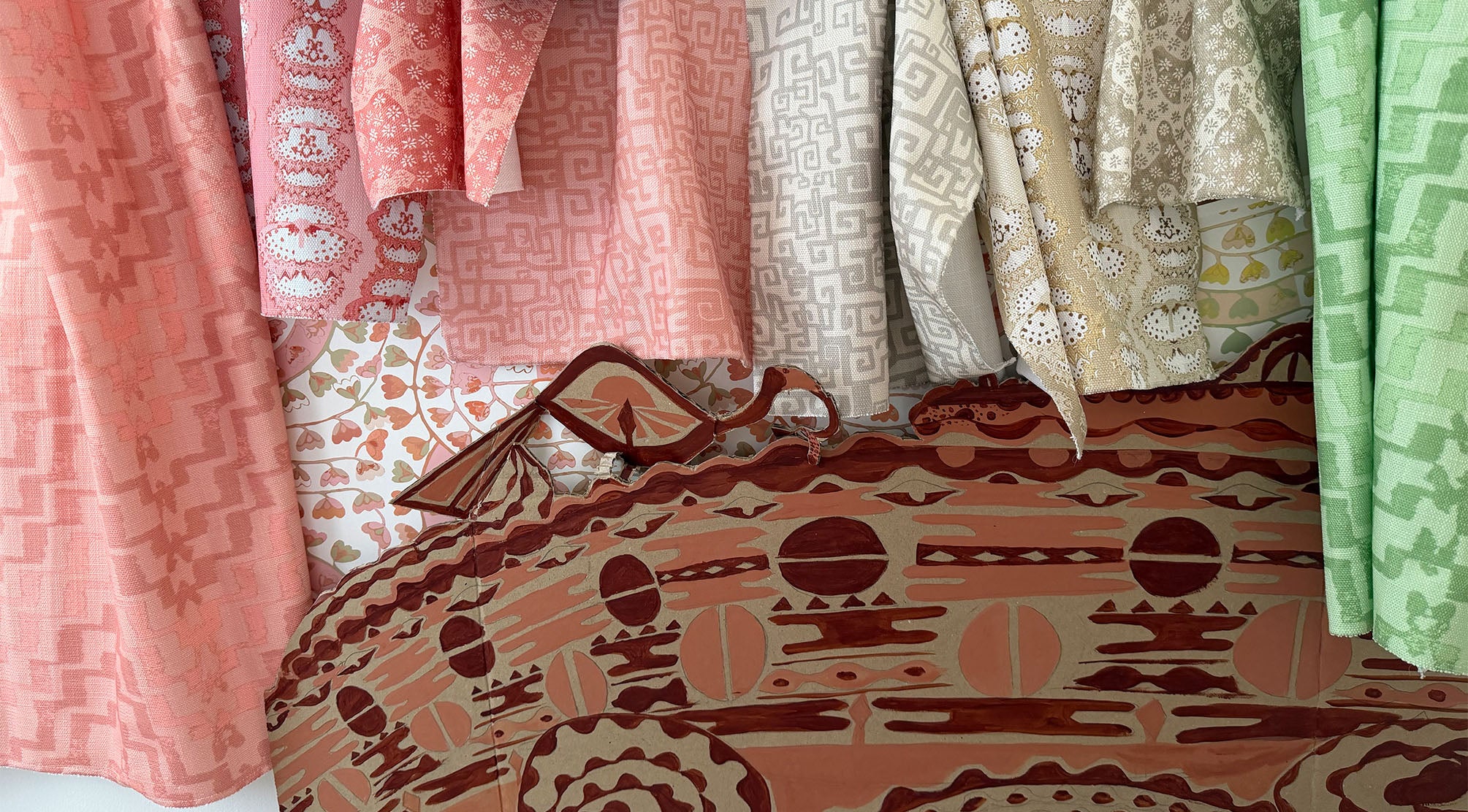 Draped fabric swatches in pink, beige and green against a hand painted screen.