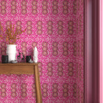 Interior with bright pink geometric wallpaper and matching trim with a wooden console table with white ceramic vases and mini ceramic sculptures. 