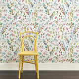 A yellow chair stands in front of a wall papered in a painterly leaf print in purple, blue, green and white.