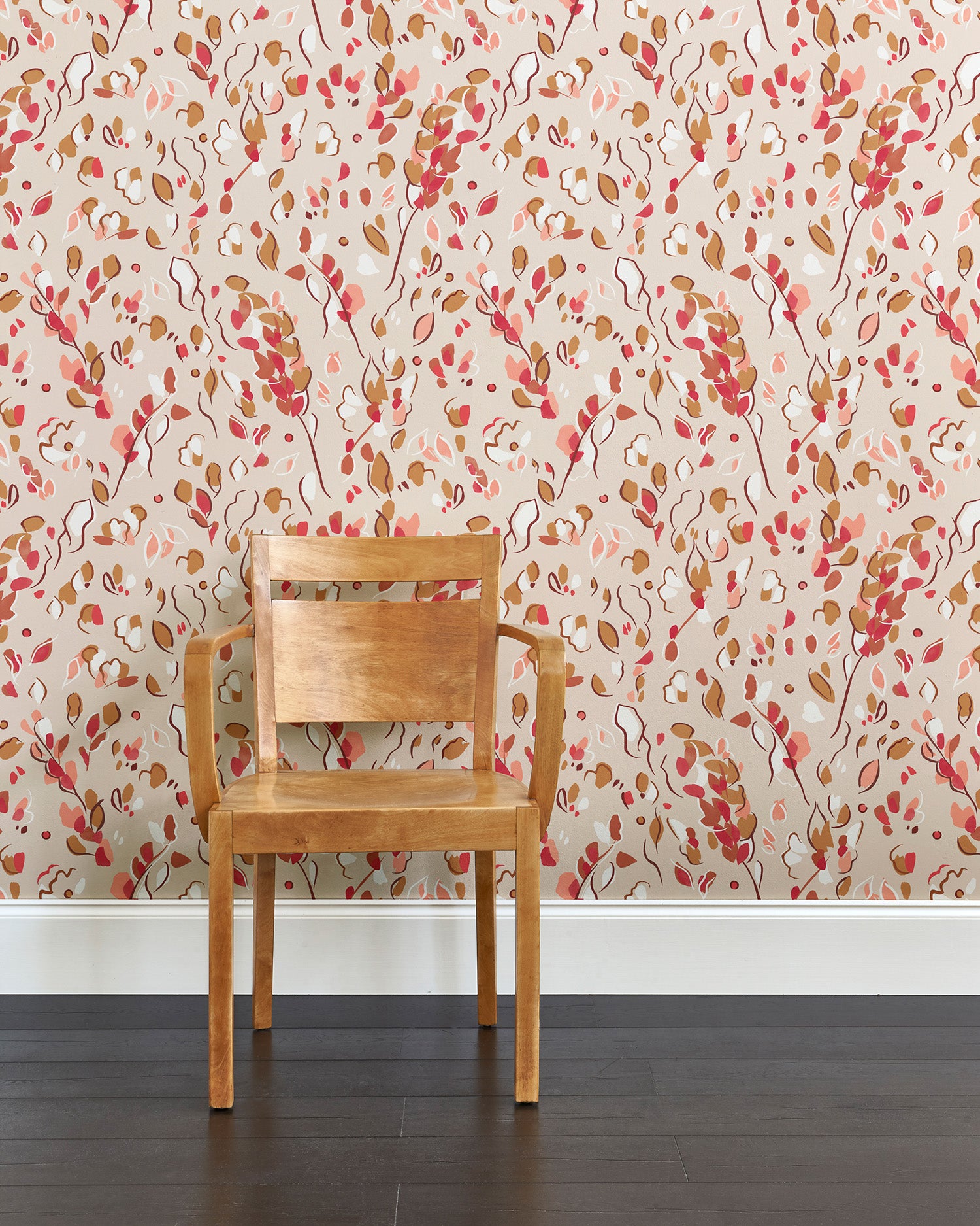 A wooden chair stands in front of a wall papered in a painterly leaf print in pink, brown and tan.