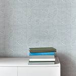 An end table with a stack of books stands in front of a wall papered in a dense herringbone print in light blue and white.