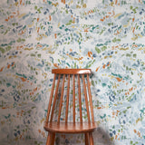 A wooden chair stands in front of a wall papered in a dappled abstract print in shades of blue, green, orange and white.