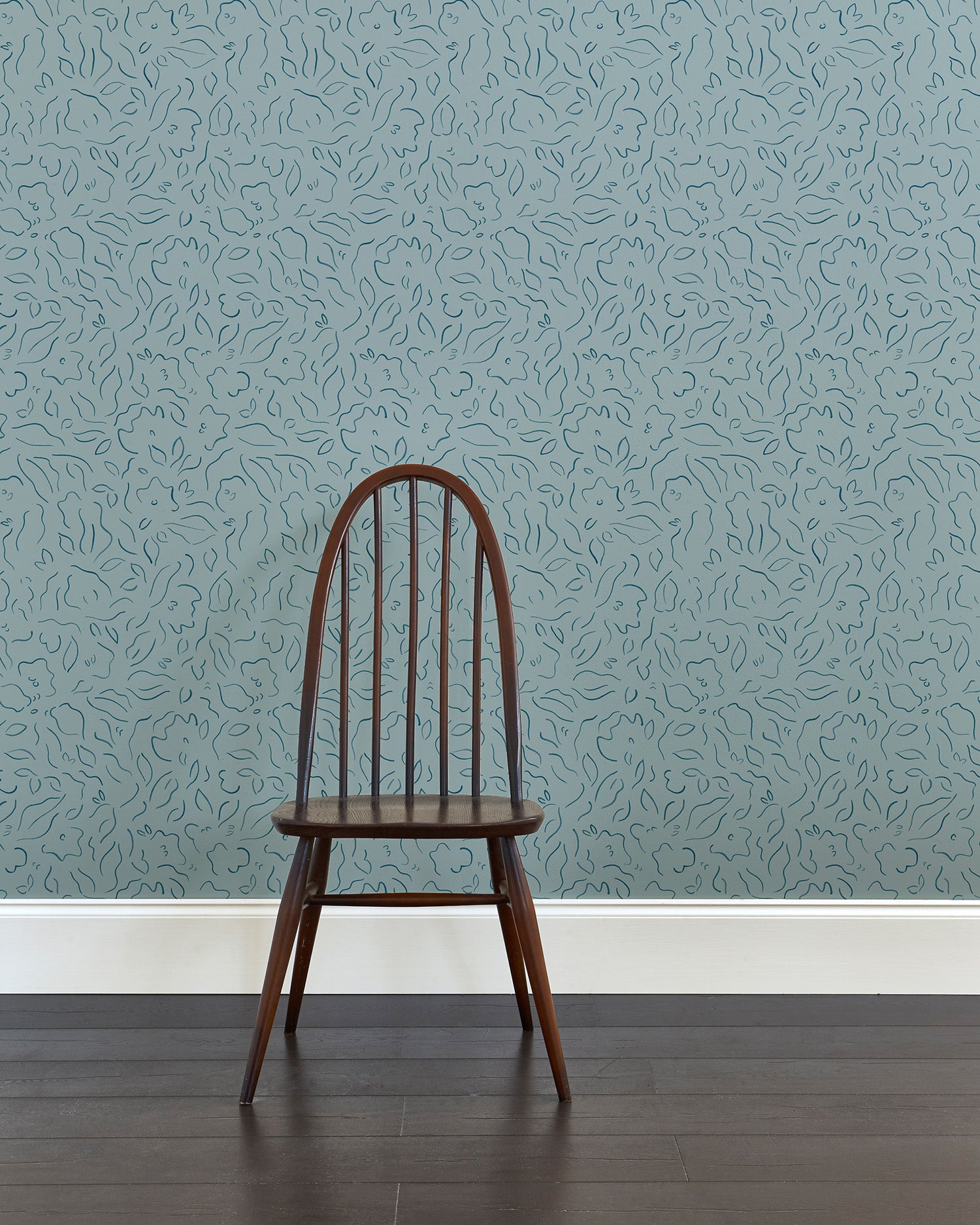 A wooden chair stands in front of a wall papered in a minimalist floral print in navy on a blue field.