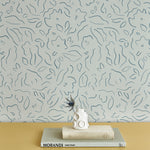 A stack of books and vase stand in front of a wall papered in a minimalist floral print in navy on a turquoise field.