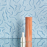 Two vases stand in front of a wall papered in a painterly floral print in blue and white on a light blue field.