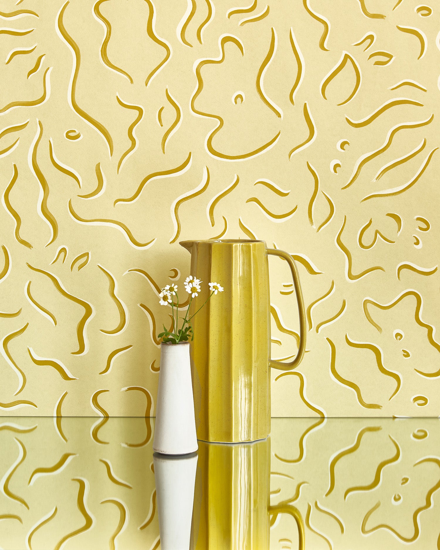 Two vases stand in front of a wall papered in a painterly floral print in yellow and white on a light yellow field.