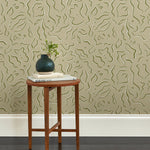 A wooden end table stands in front of a wall papered in a painterly floral print in sage and white on a light green field.