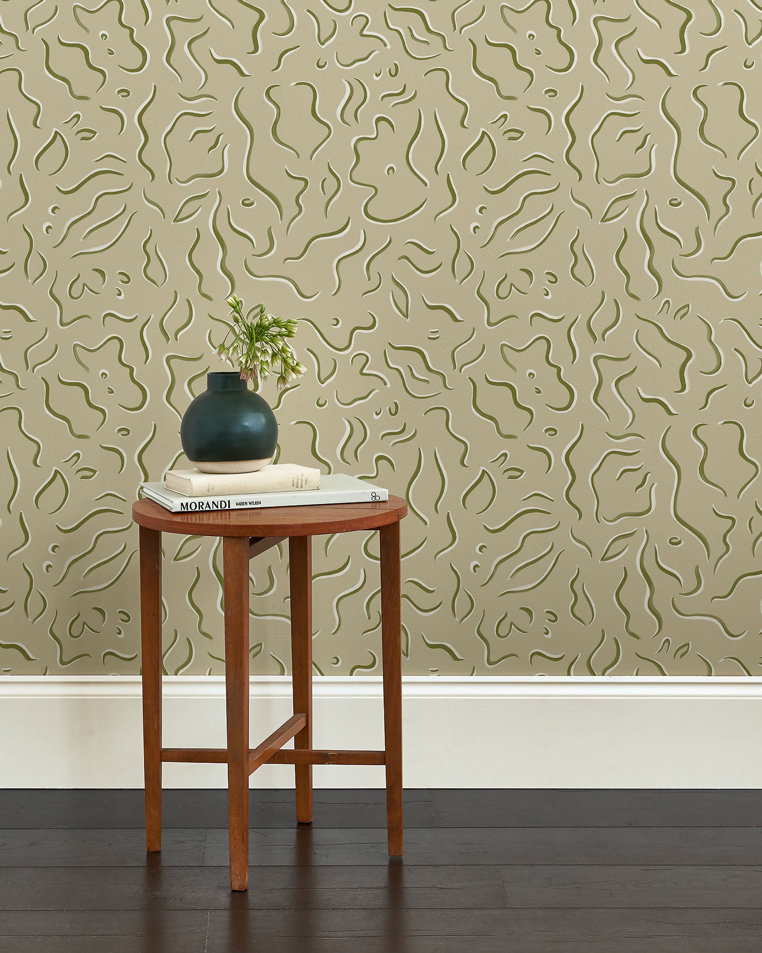 A wooden end table stands in front of a wall papered in a painterly floral print in sage and white on a light green field.