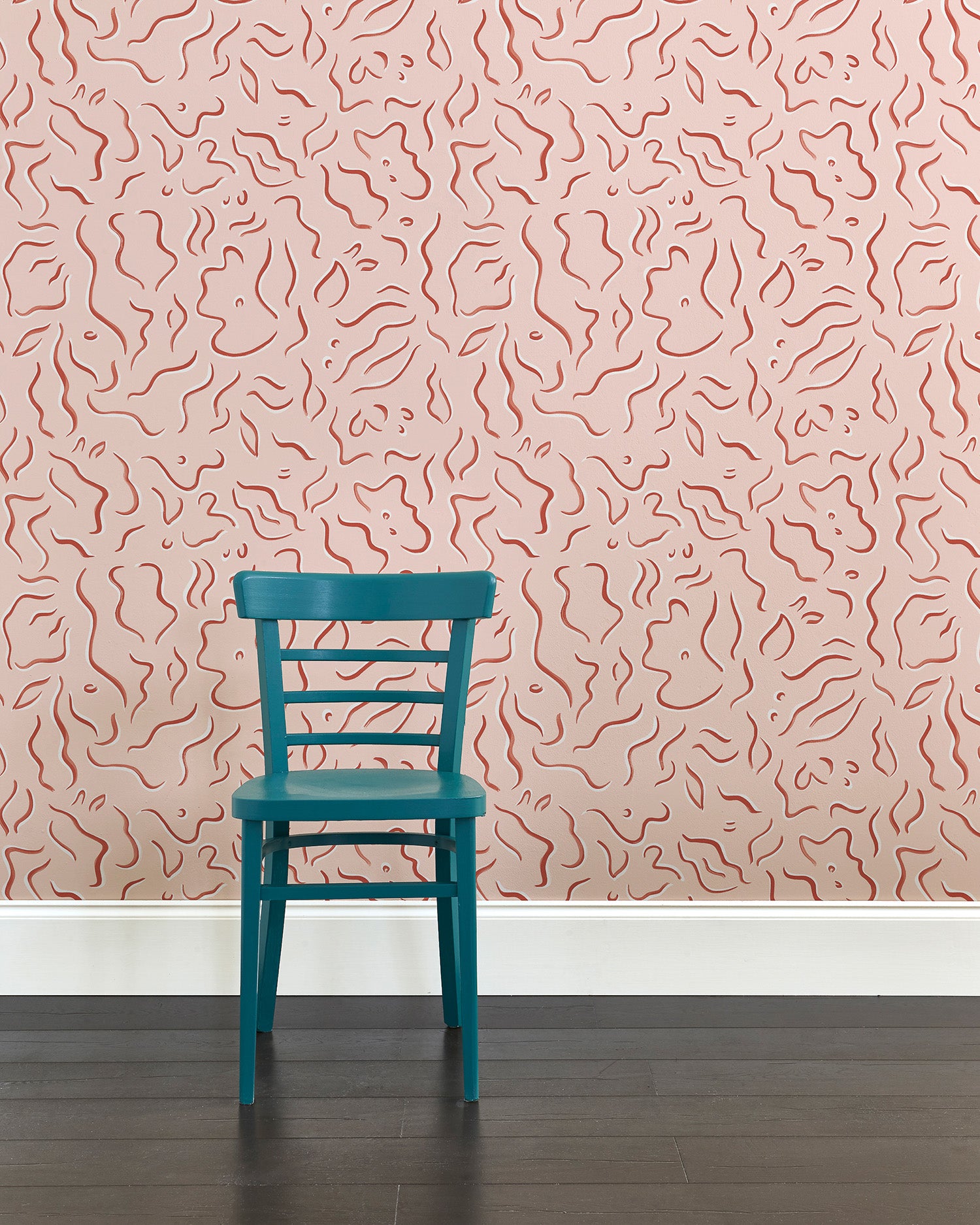 A wooden chair stands in front of a wall papered in a painterly floral print in rust and white on a light pink field.