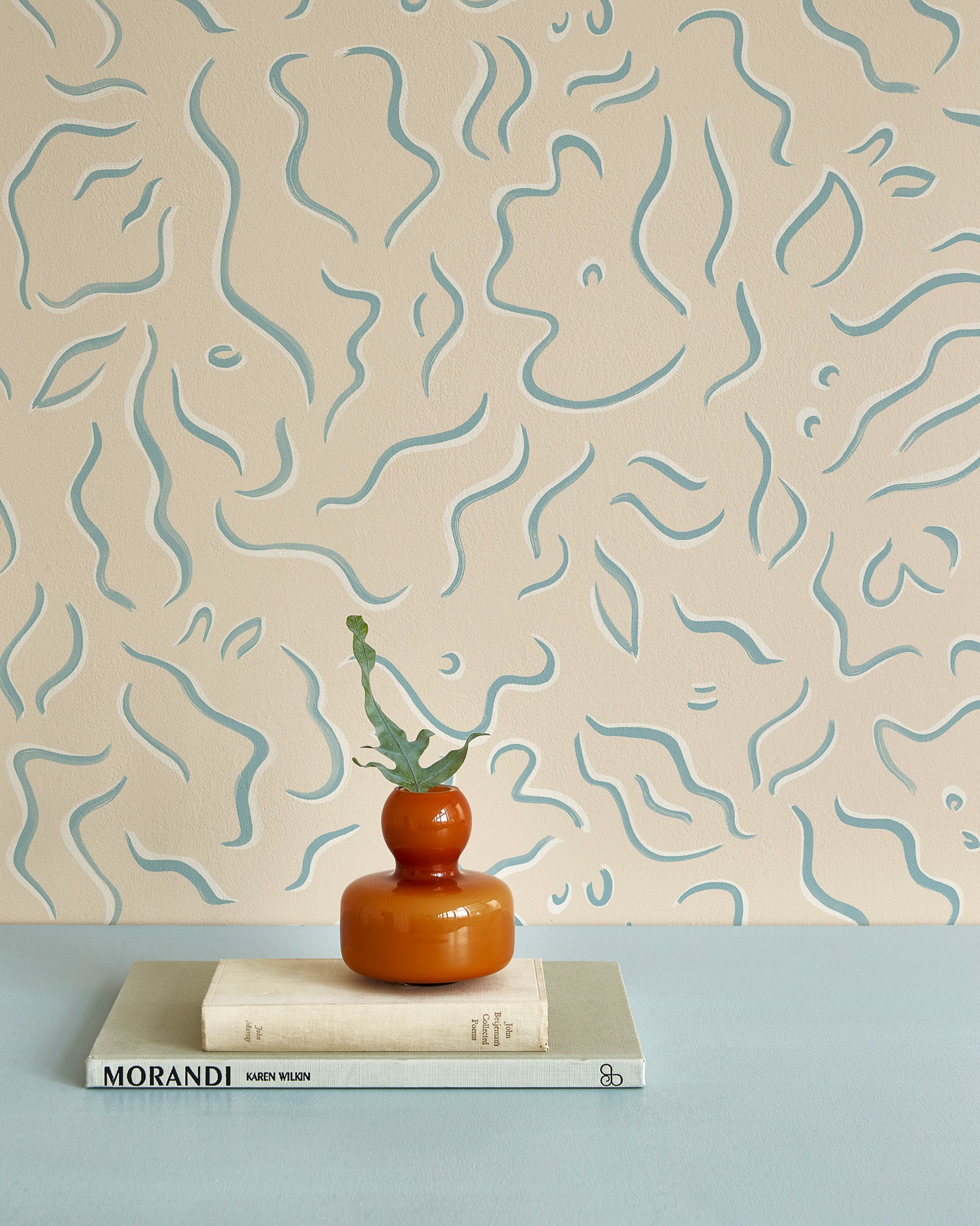 A stack of books in front of a wall papered in a painterly floral print in blue and white on a tan field.