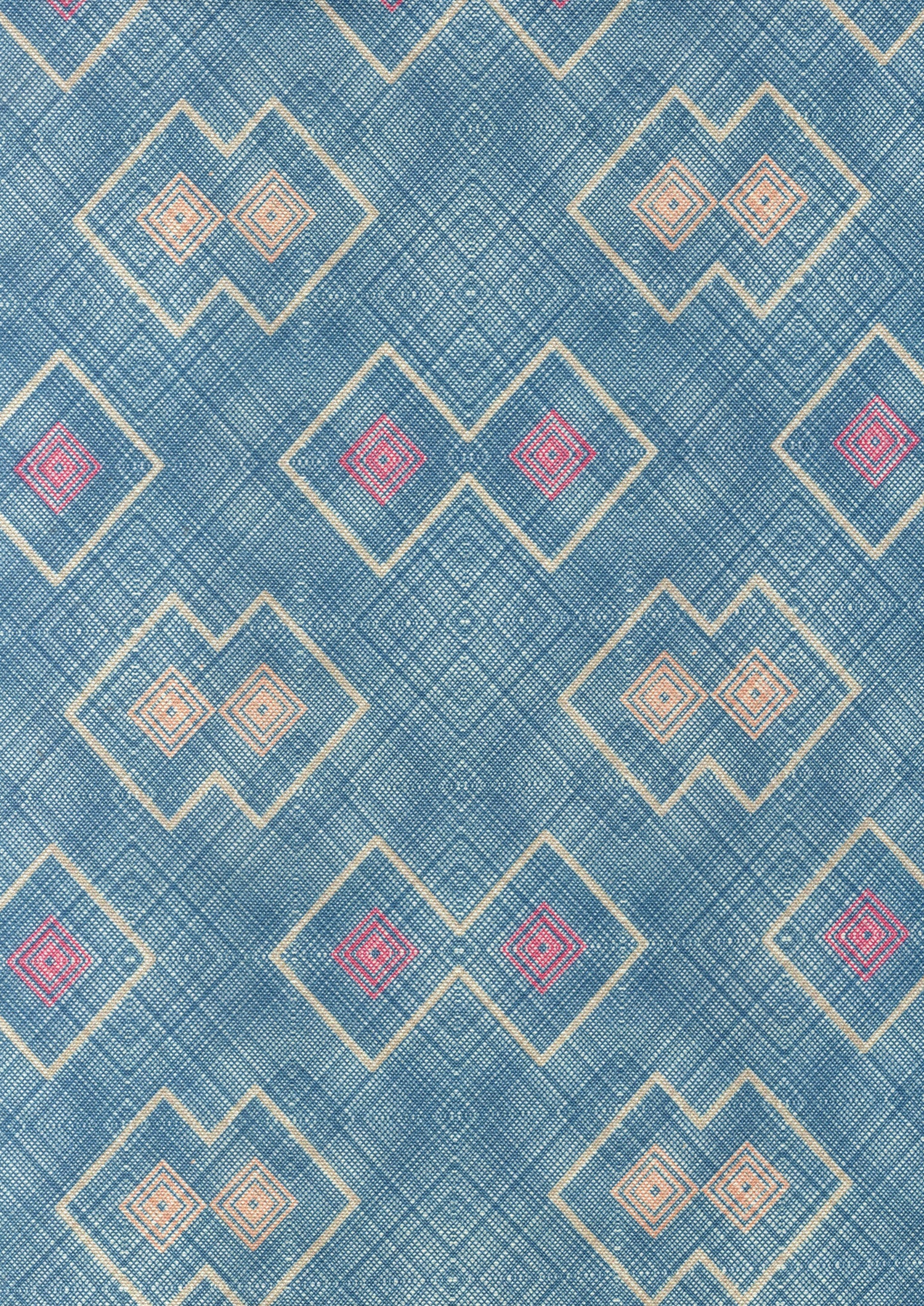 Detail of fabric in a detailed diamond lattice print in shades of red and orange on a blue field.