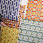 Detail image of various bold geometric wallpapers taped to a white wall with crown molding. 