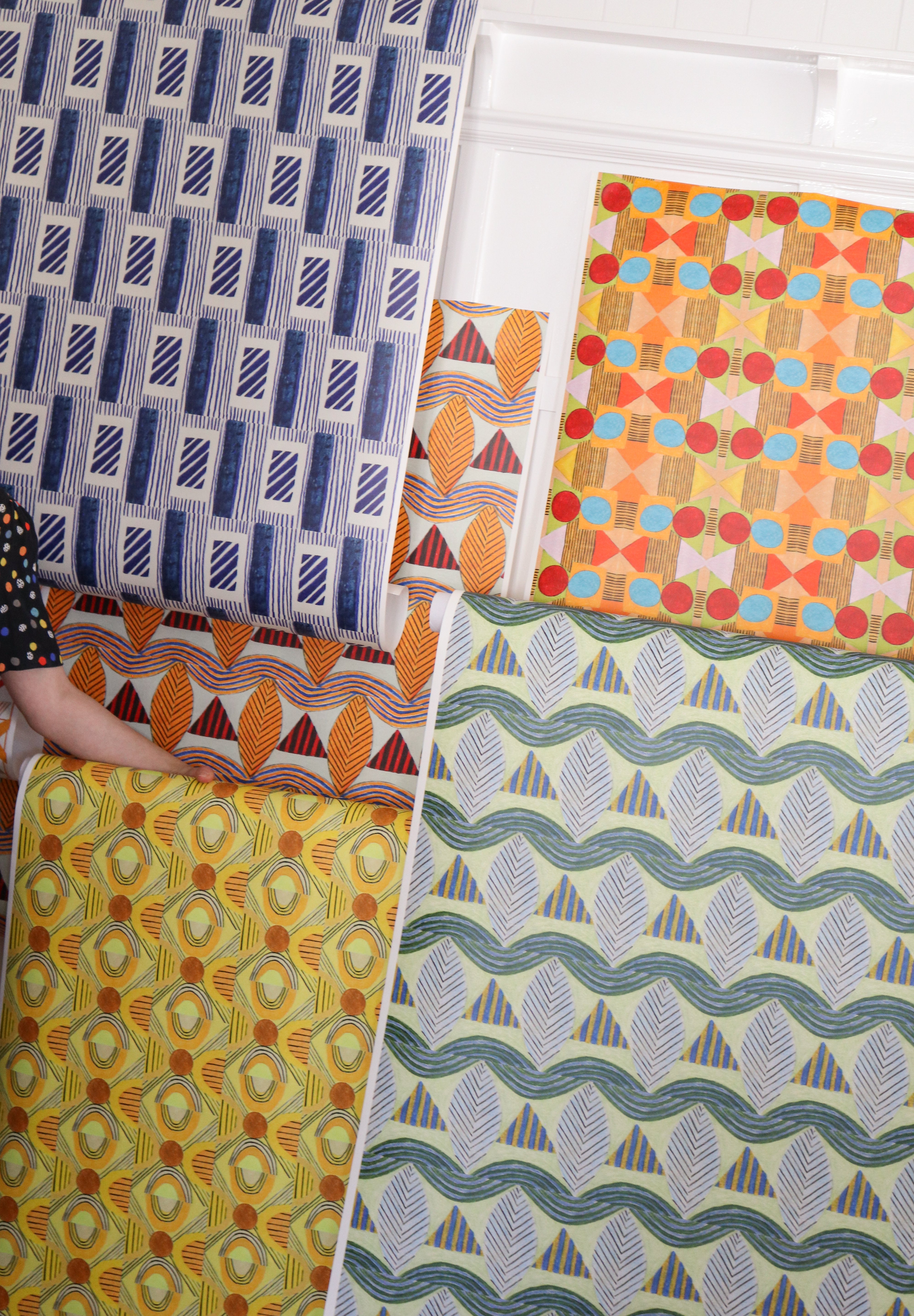 Detail image of various bold geometric wallpapers taped to a white wall with crown molding. 