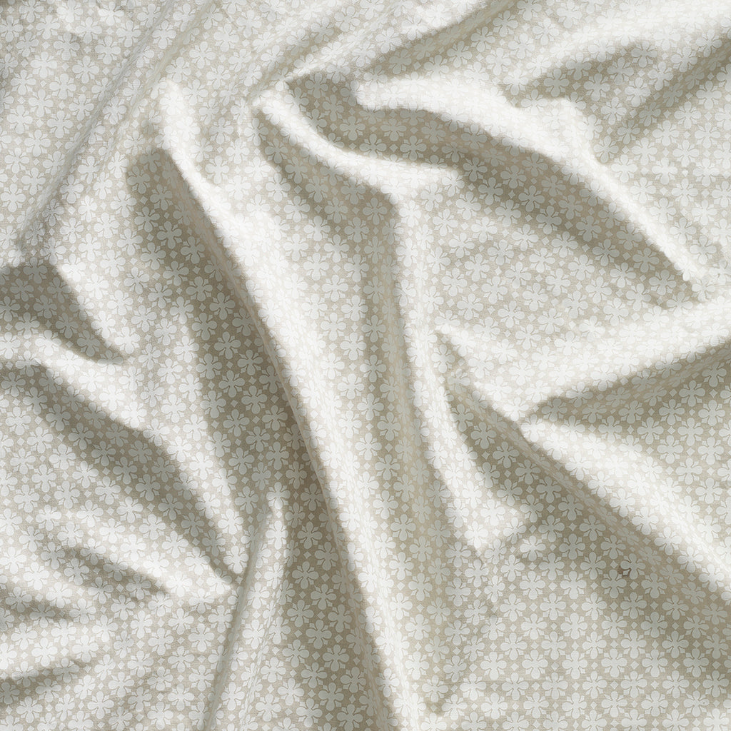 Close up of gently draped printed linen with dense floral medallion pattern in white on beige.