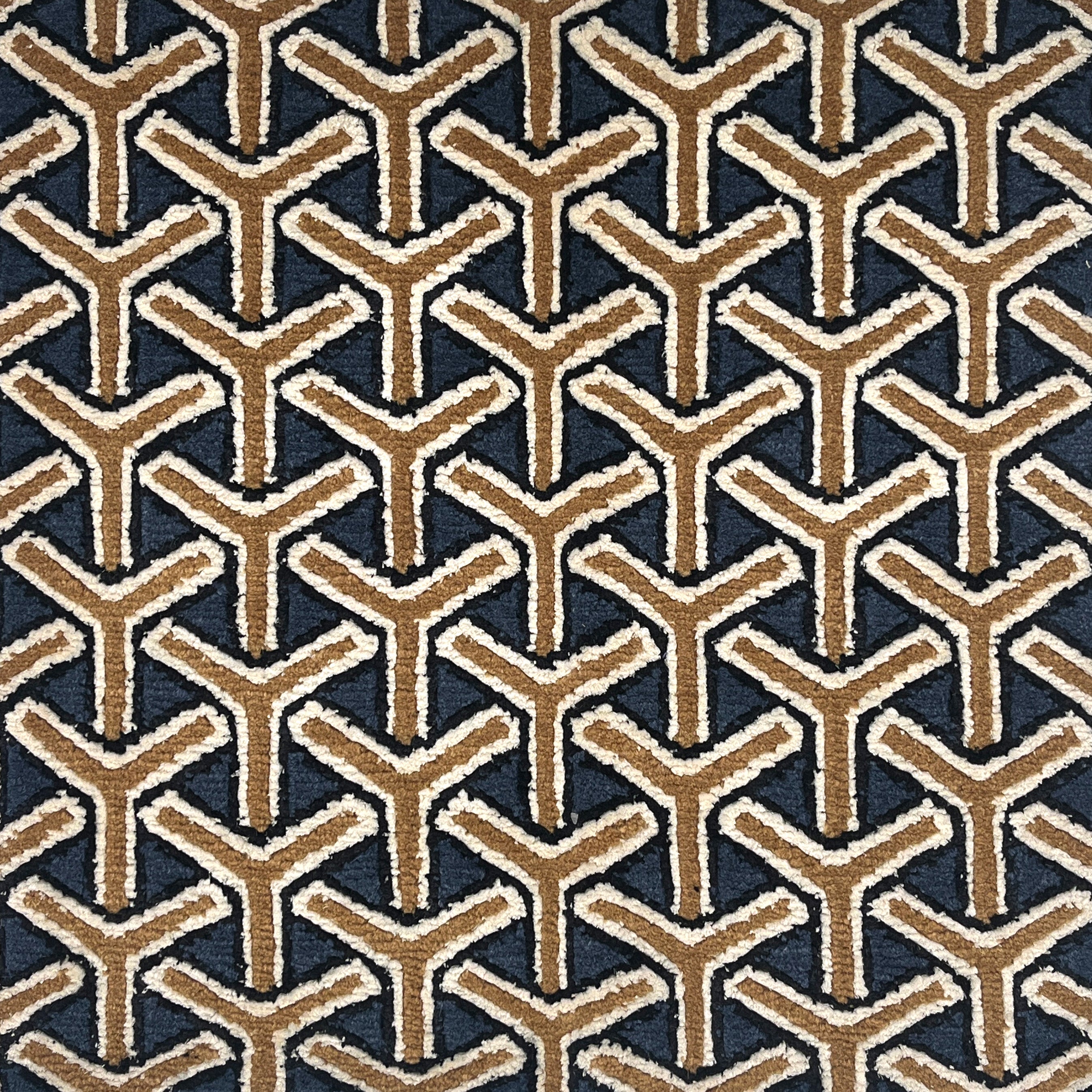 A close-up of a handknotted rug featuring a repeating geometric Y-shaped pattern in tan and off-white on a dark navy background.