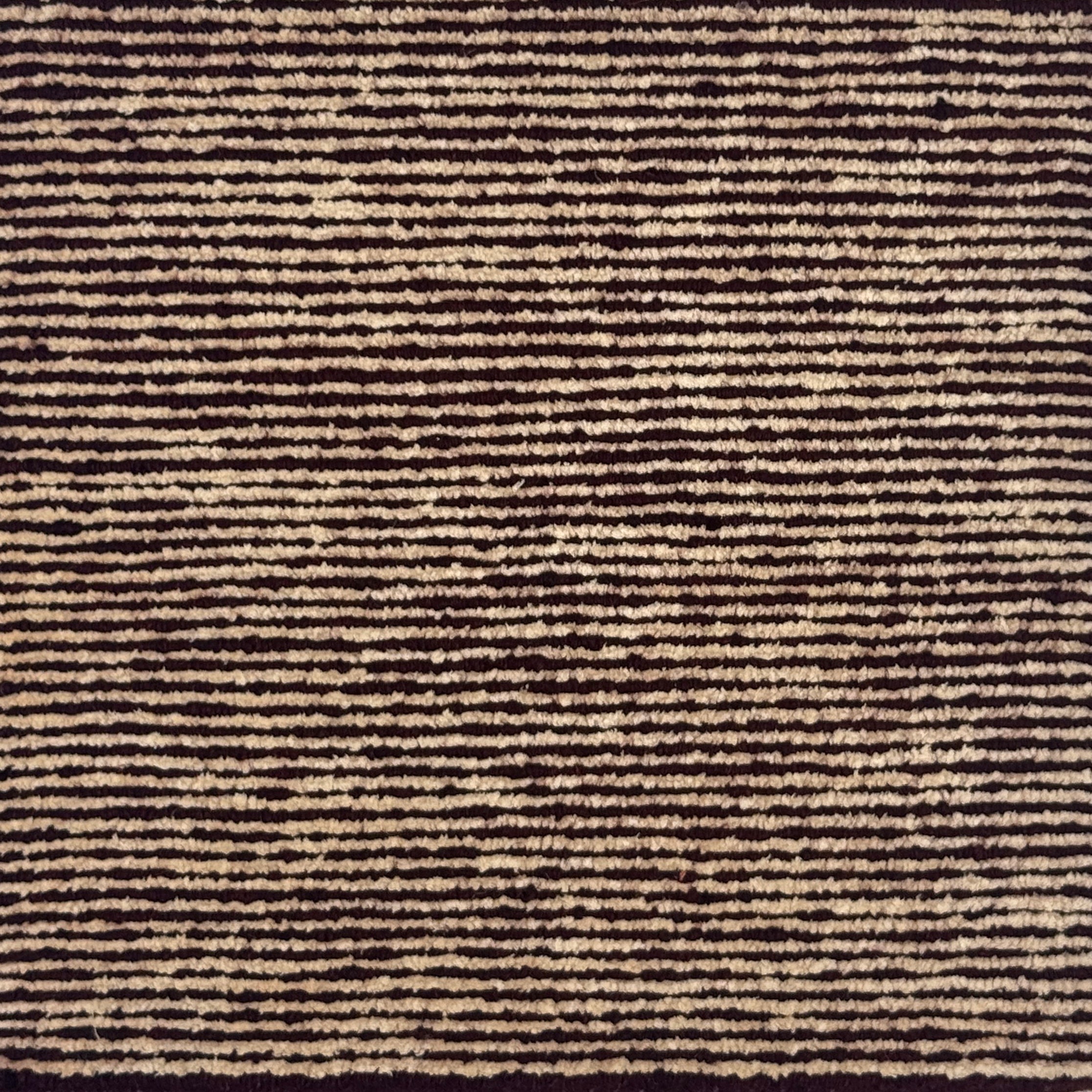 A close-up of a textured striped handknotted carpet with alternating horizontal bands of dark red and warm beige.