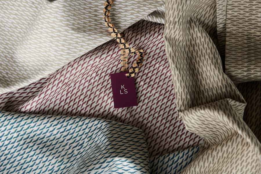 Draped fabrics in repeating abstract prints in various blue, maroon and tan colorways, with a tag labeled "KLS" on top.