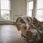 Room with a embroidered linen panel with white lips draped over a chair, large windows allowing natural light.