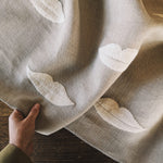 Linen with white embroidered lip pattern held by a hand on a wooden surface