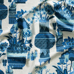 Close up of gently draped fabric in an ornate hand drawn urn and floral pattern in shades of blue on white. 