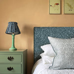 A cozy bedroom tableau with a headboard, lamp and throw pillows all upholstered in the same scrolling stem and leaf print.