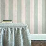 An upholstered ottoman topped with a stack of books stands in front of a wall papered in a wide stripe print.