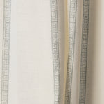 Draped printed fabric in a minimal geometric linear pattern in dusty blue on a cream field.