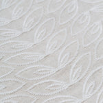 Detail of fabric with an embroidered linear leaf print in white on a white field.