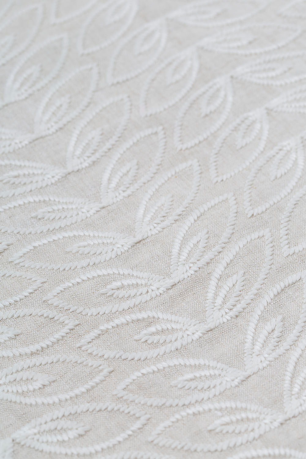 Detail of fabric with an embroidered linear leaf print in white on a white field.