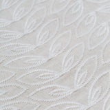Detail of fabric with an embroidered linear leaf print in white on a white field.