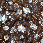 Close up of gently draped printed fabric in scrolling floral vine pattern in shades of blue, tan and taupe on a chocolate brown field. 