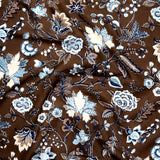 Close up of gently draped printed fabric in scrolling floral vine pattern in shades of blue, tan and taupe on a chocolate brown field. 