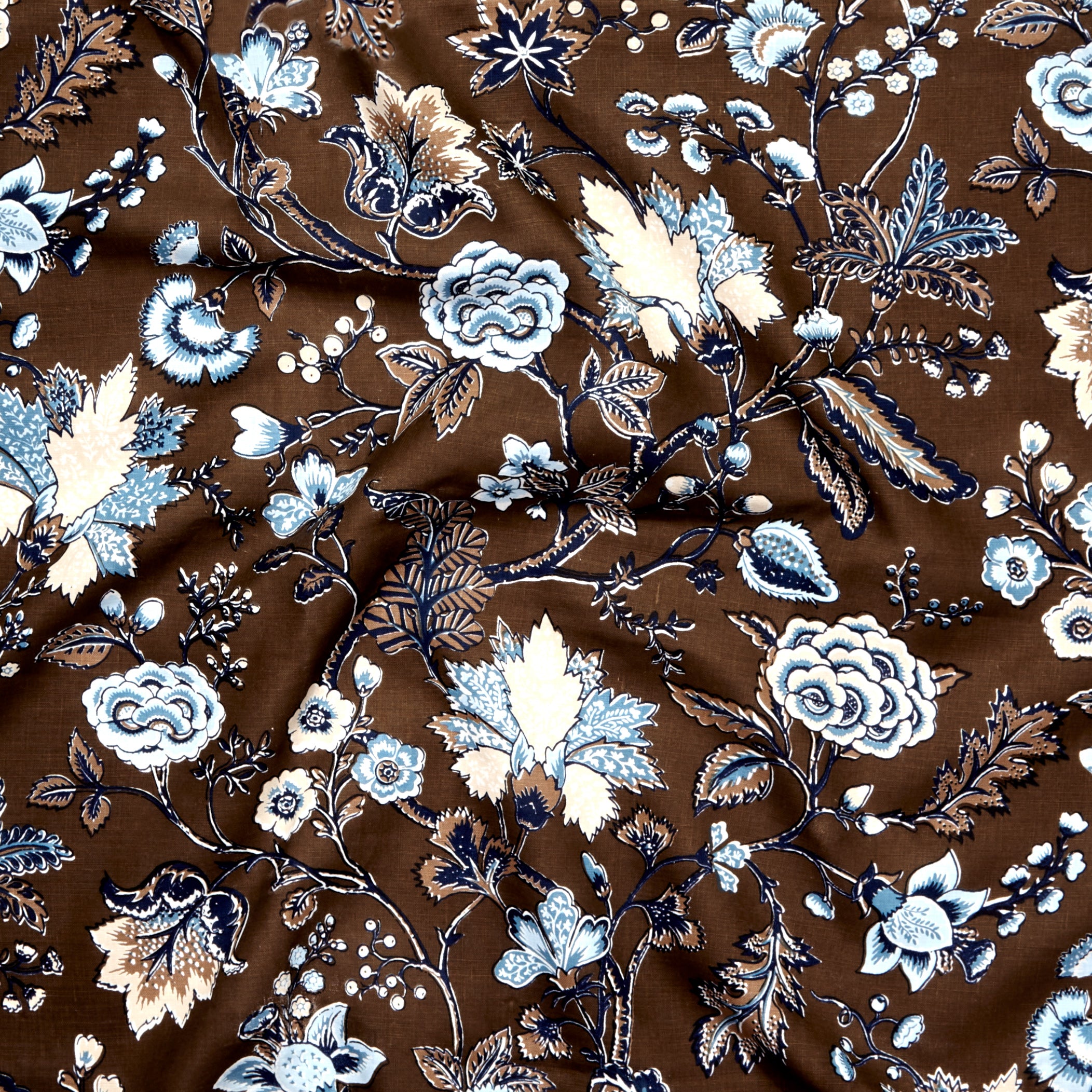 Close up of gently draped printed fabric in scrolling floral vine pattern in shades of blue, tan and taupe on a chocolate brown field. 