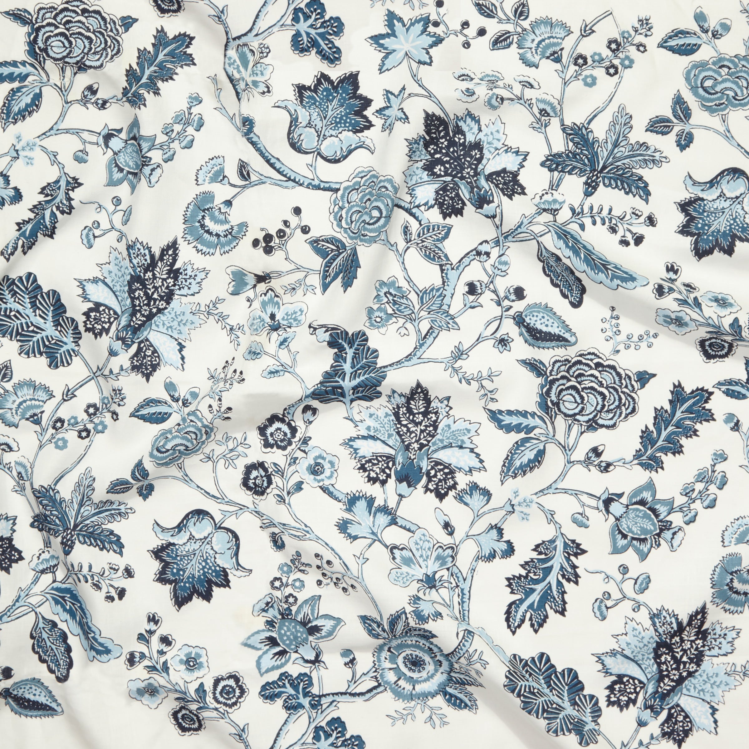 Close up of gently draped printed fabric in scrolling floral vine pattern in monochromatic blues on white. 