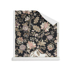 Roll of wallpaper in scrolling floral vine pattern in dark purple, blush pink, tan and brown on black.