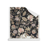 Roll of wallpaper in scrolling floral vine pattern in dark purple, blush pink, tan and brown on black.
