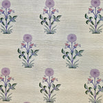 Detail of fabric in a large-scale marigold print in purple, pink and green on a tan field.