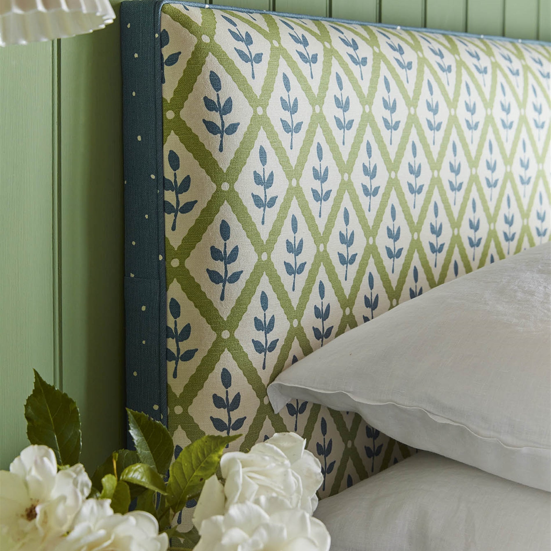 Detail of a cozy bed with a headboard upholstered in a navy and green leaf lattice print.